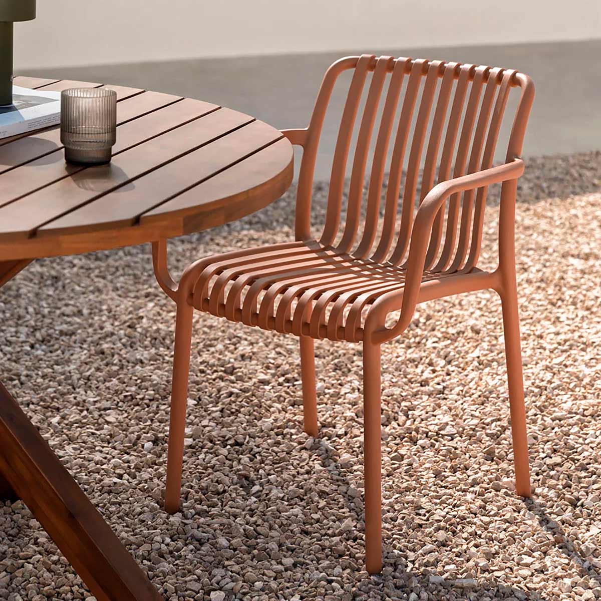 Silla de Exterior Menorca naranja  vista en perspectiva frontal frente a mesa de madera, sobre patio de piedras