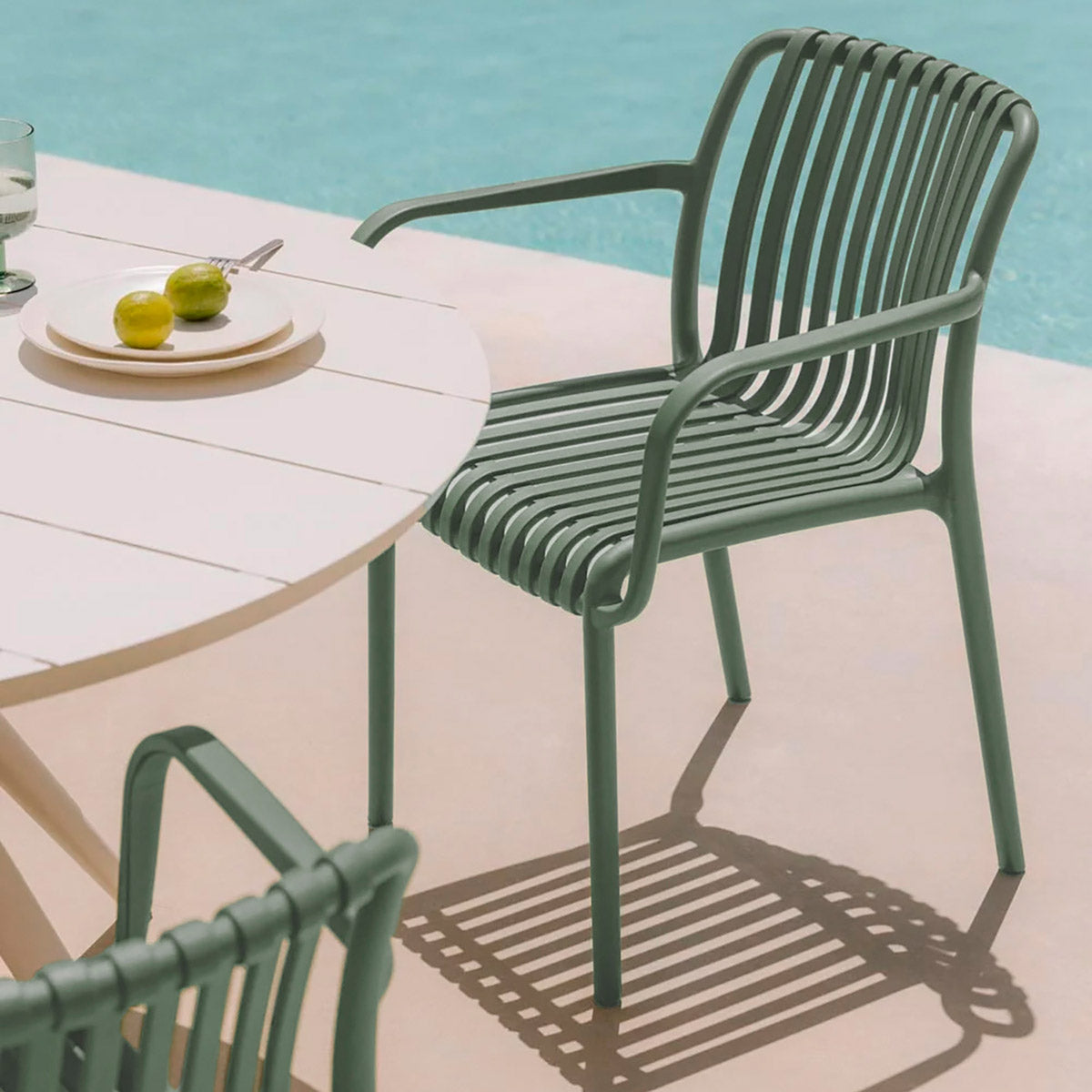 Montaje de dos Sillas de Exterior Menorca verde vista en perspectiva frontal con mesa redonda de plástico con una alberca de fondo